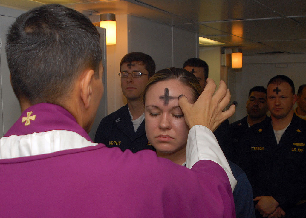 Priester zeichnet ein Aschenkreuz auf die Stirn einer jungen Frau